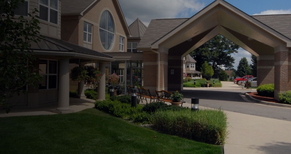 The covered entrance and landscaped front lawn of Village Manor Retirement of Hartland, a multi-storey brick building. Photograph from the community&rsquo;s own website.